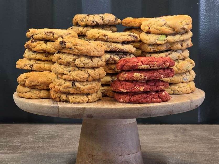 The image shows a wooden tray filled with an assortment of homemade cookies, including chocolate chip, oatmeal raisin, and red velvet varieties, neatly stacked in layers.
AI-generated content may be incorrect.