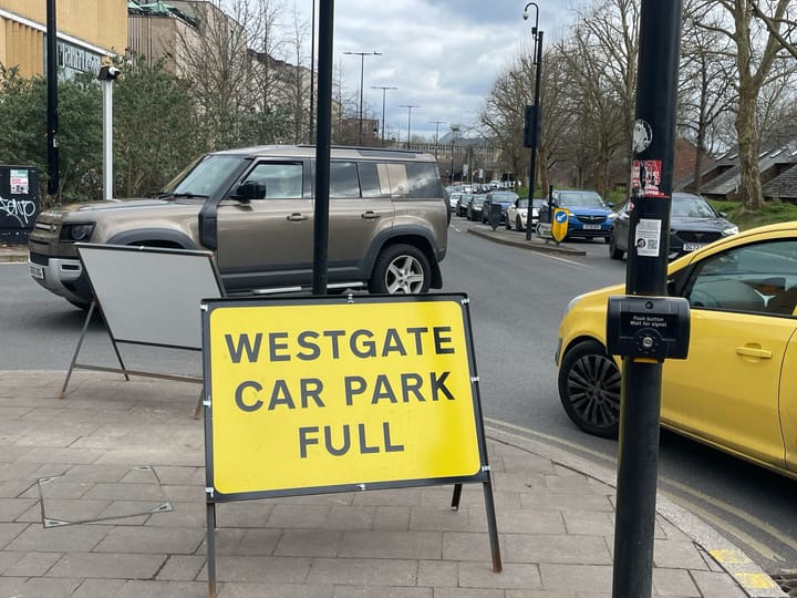 A traffic jam at the Westgate car park in Oxford where the sign reads 'car park full' and a large off-vehicle waits to enter.